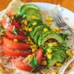 A taco with sliced tomatoes, corn, and avocado.