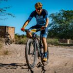 A man on a bike is riding on a dirt trail while wearing cyclist attire.