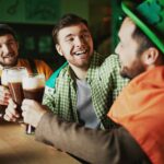 Three men dressed in St. Patrick’s Day attire are raising three glasses of Guinness beer at a bar.